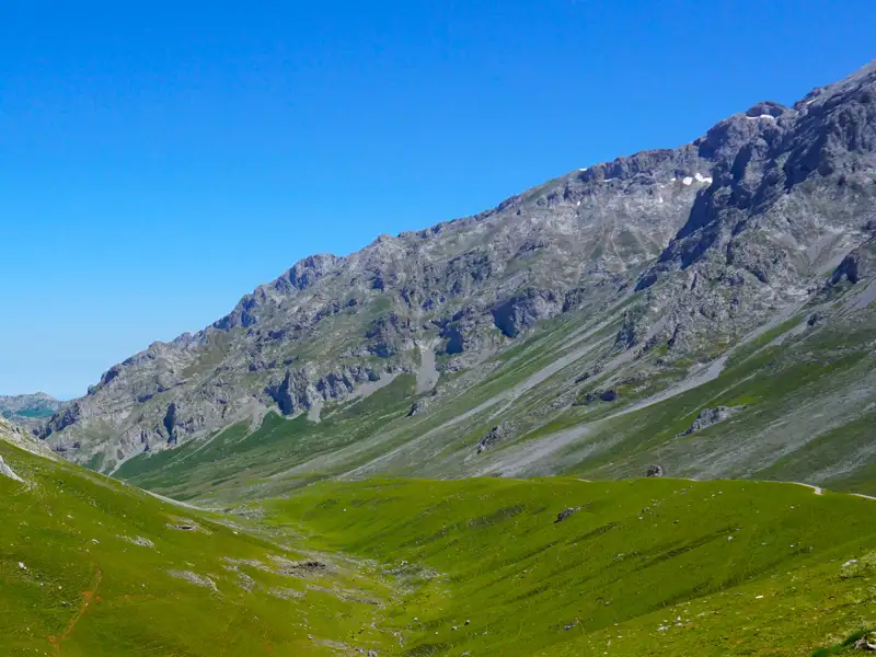 Grüne Hänge und felsige Gipfel eines Gebirges unter blauem Himmel.