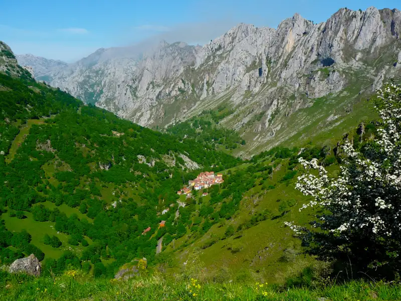 Blick auf ein Bergdorf inmitten eines grünen Tals, umgeben von hohen Bergen.