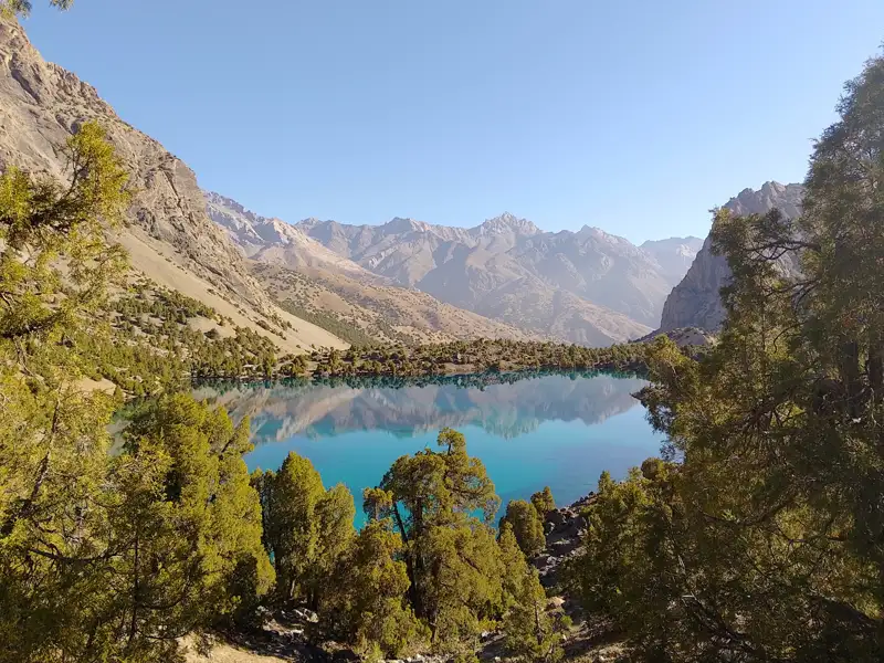 Ein klarer Bergsee, umgeben von Bäumen und Bergen.