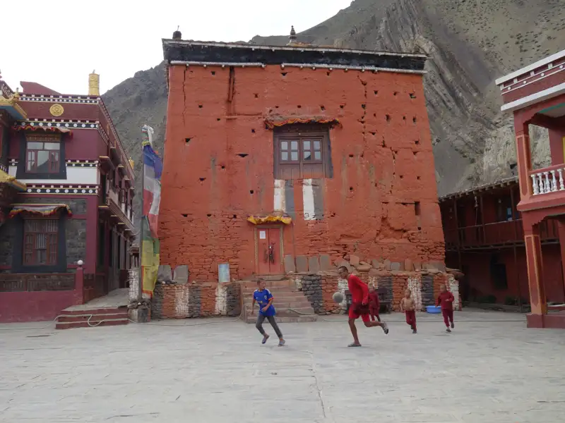 Kinder spielen Fußball vor einem roten Gebäude, das Teil einer kulturellen Stätte sein könnte.