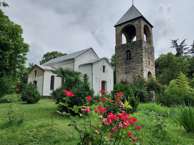 Historische Kirche mit separatem Glockenturm und blühendem Rosengarten.