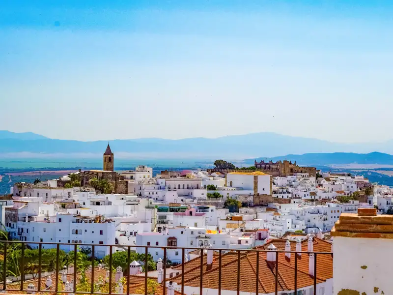 Panoramablick auf die weißgetünchte Stadt mit Kirche und Burg, umgeben von einer hügeligen Landschaft.