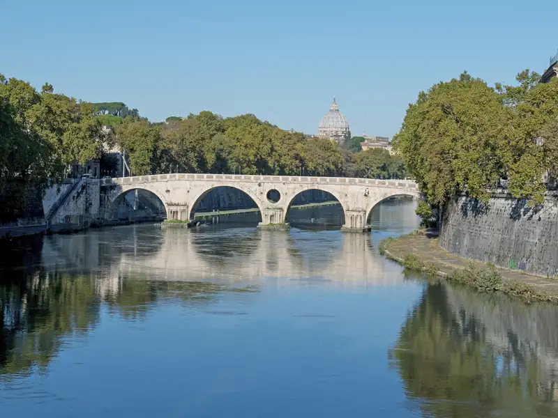 Historische Brücke über den Tiber in Rom mit dem Petersdom im Hintergrund.