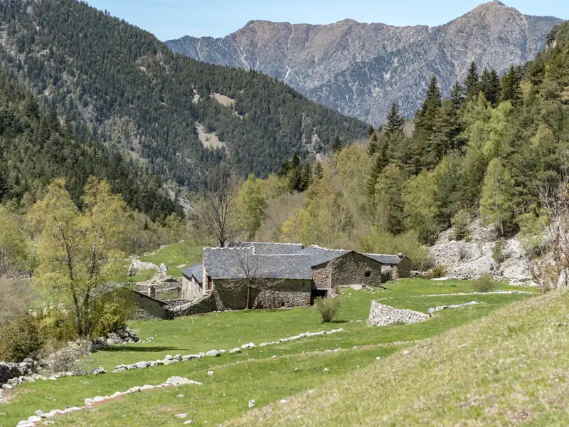 Traditionelles Steinhaus inmitten eines grünen Tals, umgeben von den bewaldeten Pyrenäen.