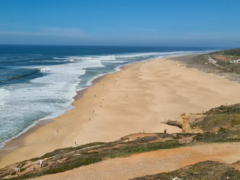 Panoramablick auf einen Sandstrand mit einlaufenden Wellen.