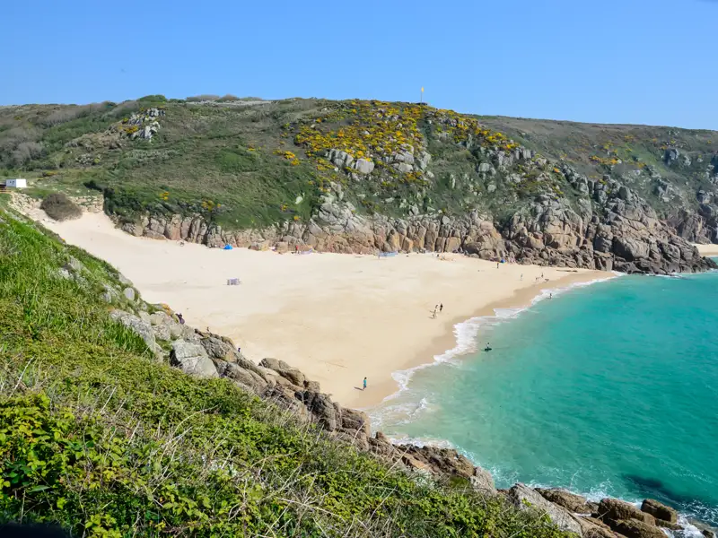 Türkisfarbenes Wasser und weißer Sandstrand umgeben von grünen Hügeln.