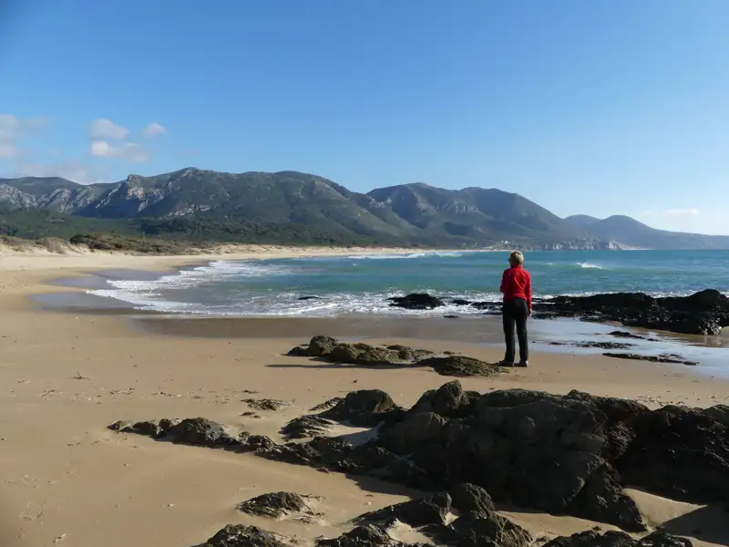 Person am Strand mit Blick auf Meer und Berge.