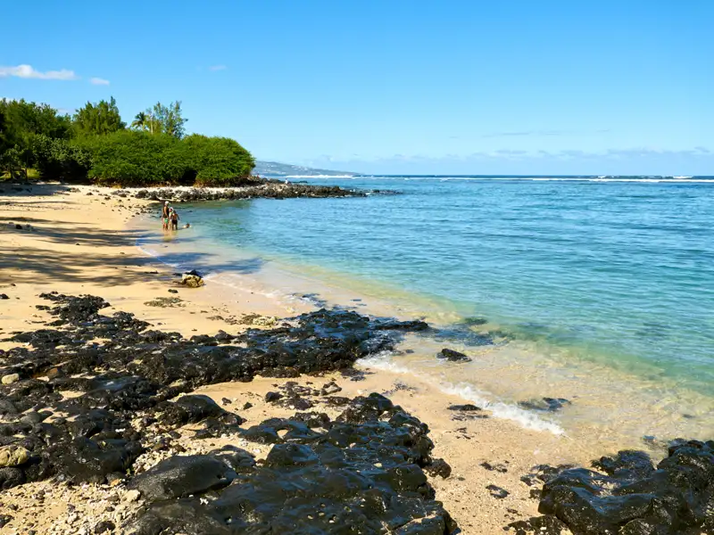 Strand mit schwarzem Vulkangestein und türkisfarbenem Wasser.
