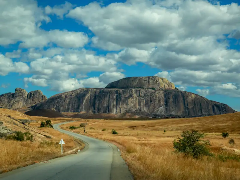 Eine Straße führt durch eine savannenartige Landschaft zu imposanten Felsformationen.