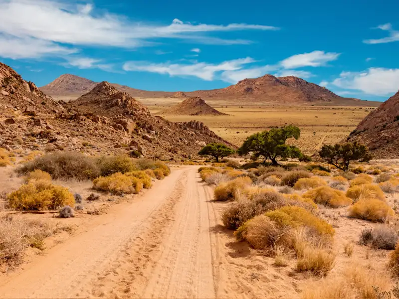 Unbefestigte Straße in einer trockenen, bergigen Landschaft.
