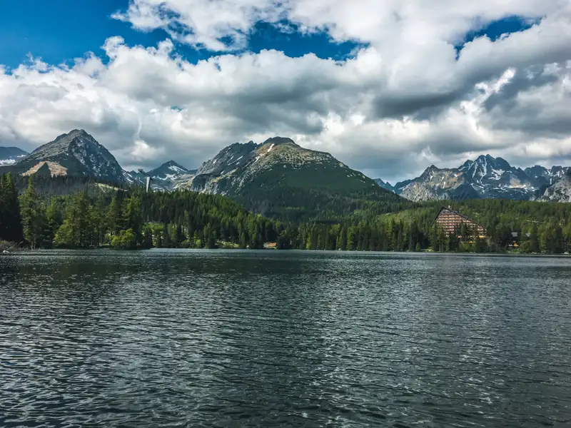 Ansicht eines Bergsees mit einem Hotel am Ufer und Bergen im Hintergrund.
