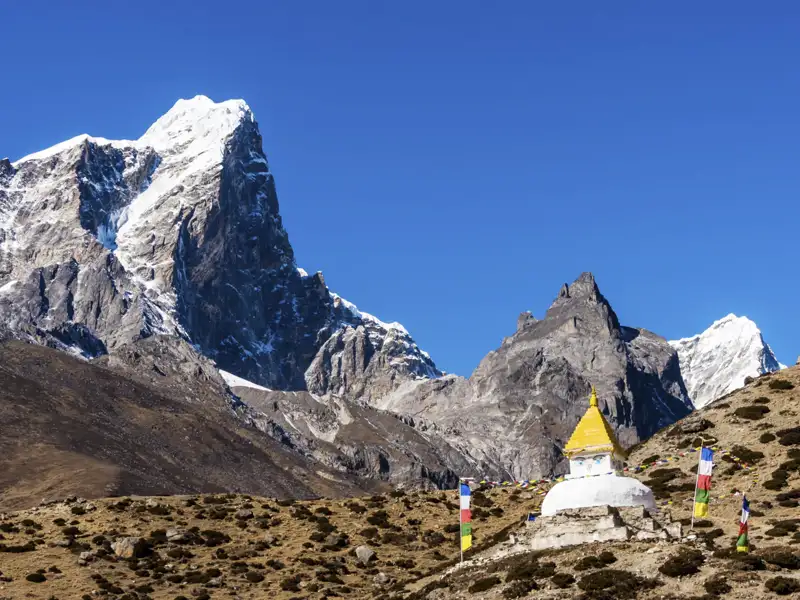 Gebetsfahnen und eine Stupa vor der beeindruckenden Kulisse des Himalayas.