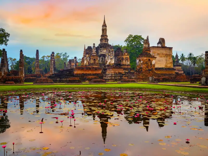 Ruinen einer historischen Tempelanlage mit Wasserbecken und Seerosen im Vordergrund bei Sonnenuntergang.
