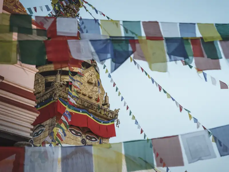 Nahaufnahme einer Stupa mit bunten Gebetsfahnen, die im Wind wehen.