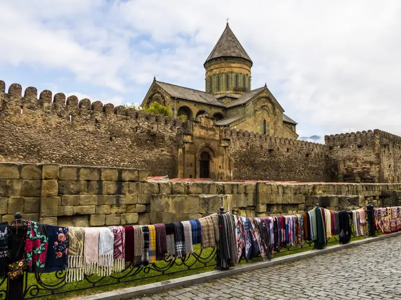 Wanderer auf einem Bergpfad in einem grünen Tal, umgeben von schneebedeckten Gipfeln.