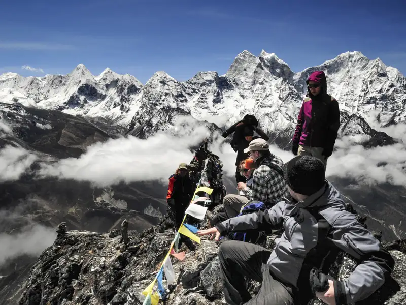 Wandergruppe auf einem Berggipfel mit Blick auf die schneebedeckten Himalaya-Gipfel.
