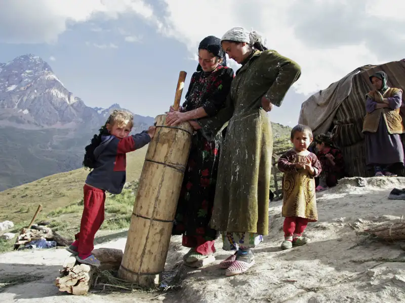 Szene des traditionellen Lebens im Gebirge: Frauen und Kinder in traditioneller Kleidung bei der Arbeit im Freien vor einem Bergpanorama.