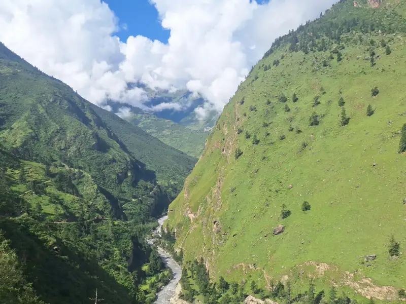 Panoramablick auf ein grünes Tal mit einem Fluss, umgeben von bewaldeten Bergen.