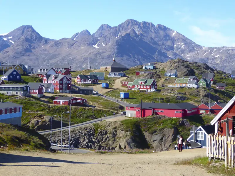 Farbenfrohe Häuser in einer grönländischen Siedlung, umgeben von einer bergigen Landschaft.