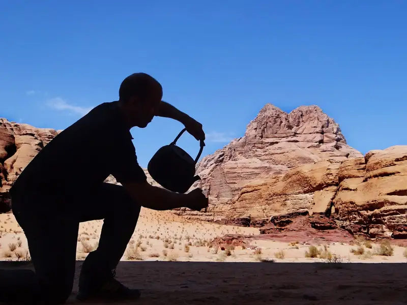 Reisender macht eine Pause und gießt Wasser aus einem Kessel in der Wüste aus.