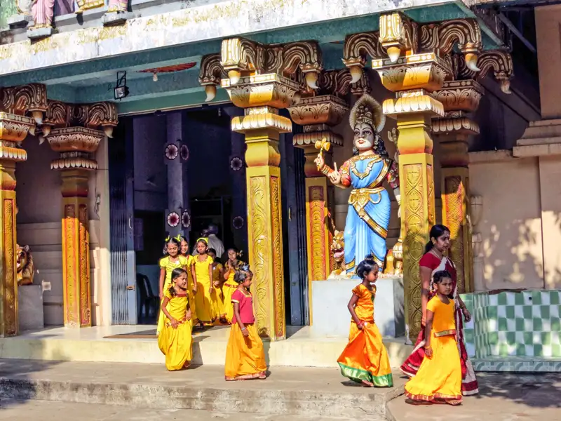 Mädchen in gelben Kleidern vor einem Tempelgebäude.