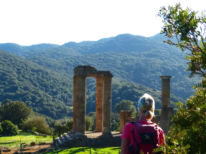 Besucher bewundert antike Säulen inmitten einer hügeligen Landschaft.