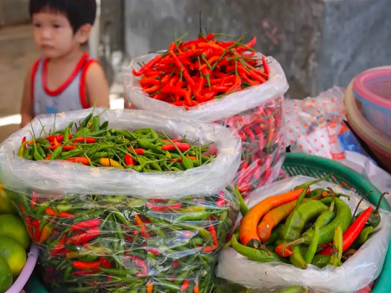 Rote und grüne Chilischoten in Plastiktüten auf einem Marktstand.