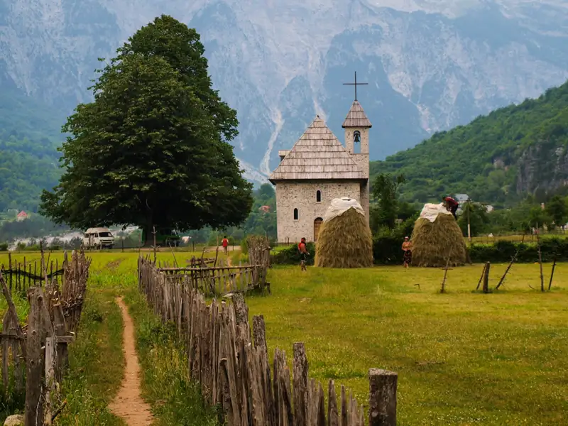 Eine kleine Kirche und Heuhaufen in einer Berglandschaft.