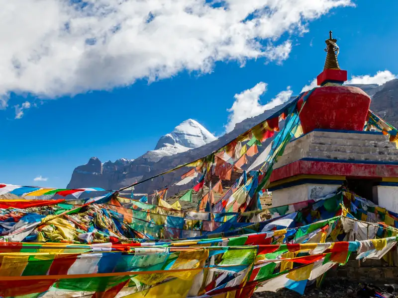 Gebetsfahnen flattern im Wind vor einer Stupa mit dem Berg Kailash im Hintergrund.