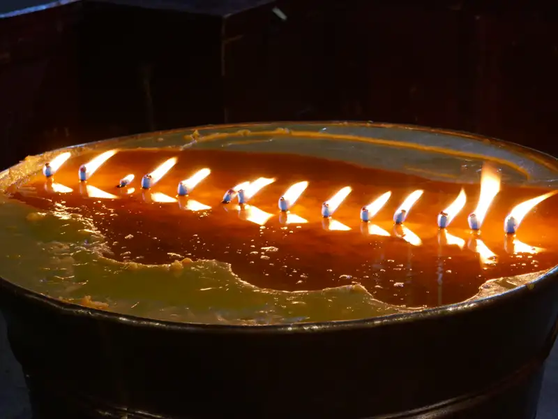 Brennende Kerzen in einem Gefäß, möglicherweise Teil eines religiösen Rituals oder einer Gedenkstätte.