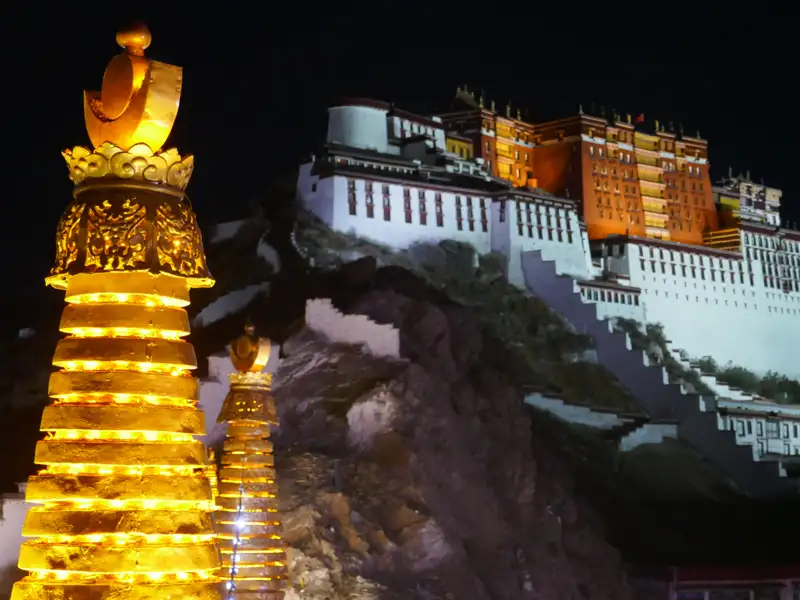 Der Potala-Palast, ein historisches Wahrzeichen Tibets, wird bei Nacht beleuchtet. Im Vordergrund befinden sich beleuchtete Stupas.