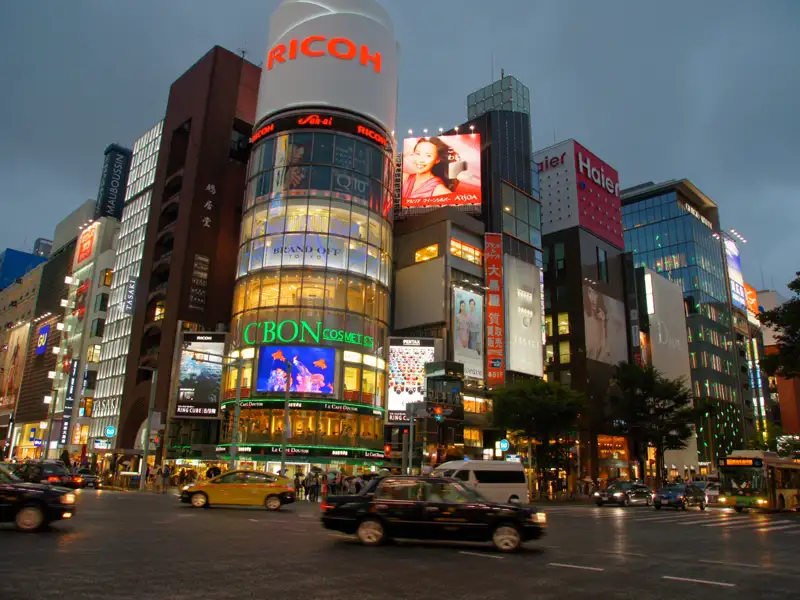 Straßenszene mit beleuchteten Gebäuden und Werbetafeln in einer japanischen Stadt.