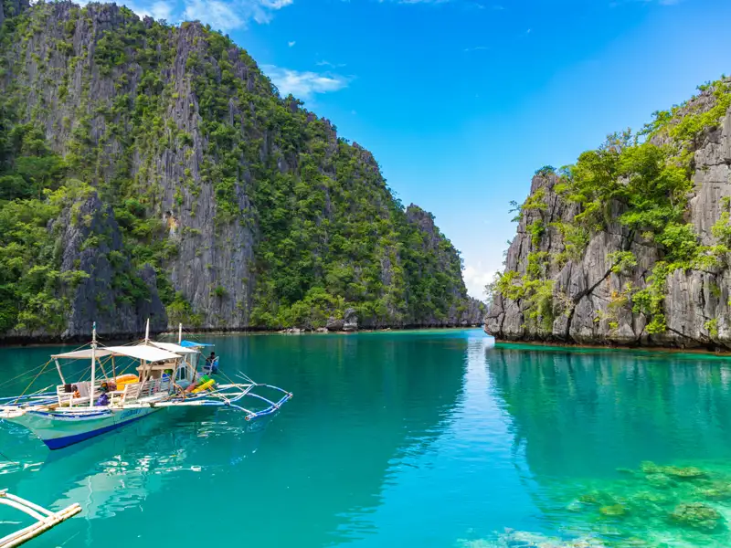 Traditionelles Auslegerboot in einer Bucht der Philippinen, umgeben von Kalksteinfelsen und türkisfarbenem Wasser.