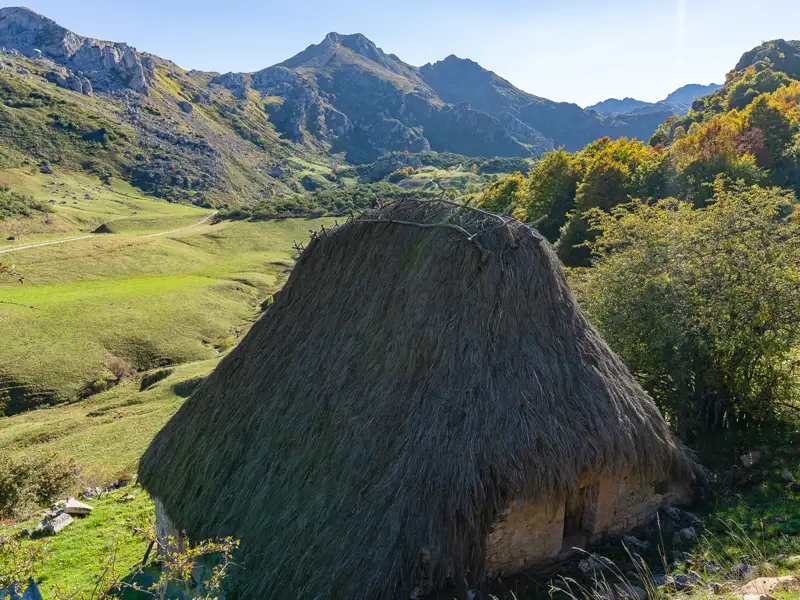 Traditionelle Hütte mit Strohdach in einer Berglandschaft.