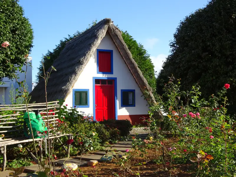Traditionelles Haus mit Strohdach und buntem Anstrich in einem Garten.