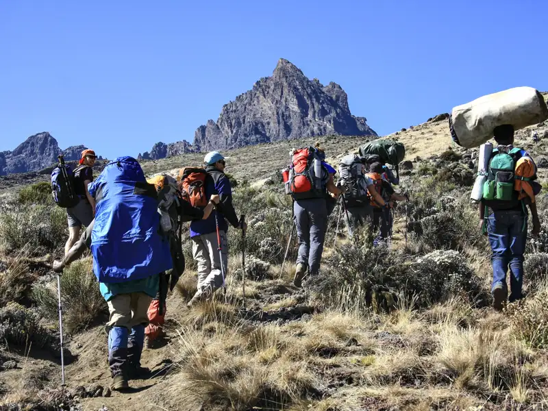 Wandergruppe auf einem Bergpfad mit Trekkingstöcken und Rucksäcken unterwegs.