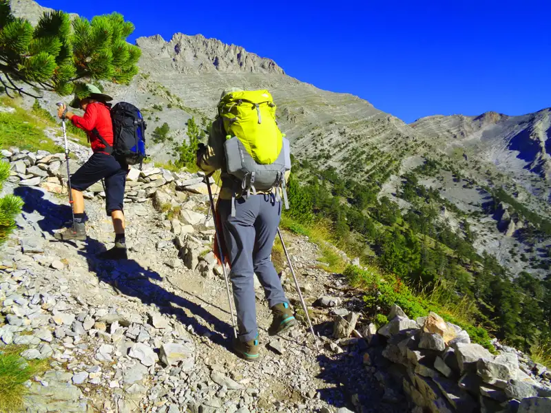 Zwei Wanderer mit Trekkingausrüstung steigen einen Bergpfad hinauf.