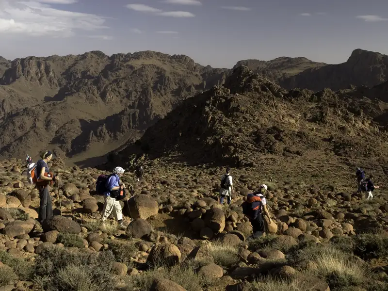 Wanderer mit Rucksäcken und Wanderstöcken in einer felsigen Berglandschaft.