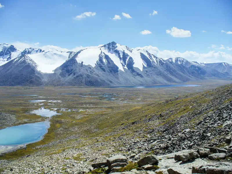 Panoramablick auf schneebedeckte Berge, Seen und ein Geröllfeld, typisch für die Landschaft der Region.