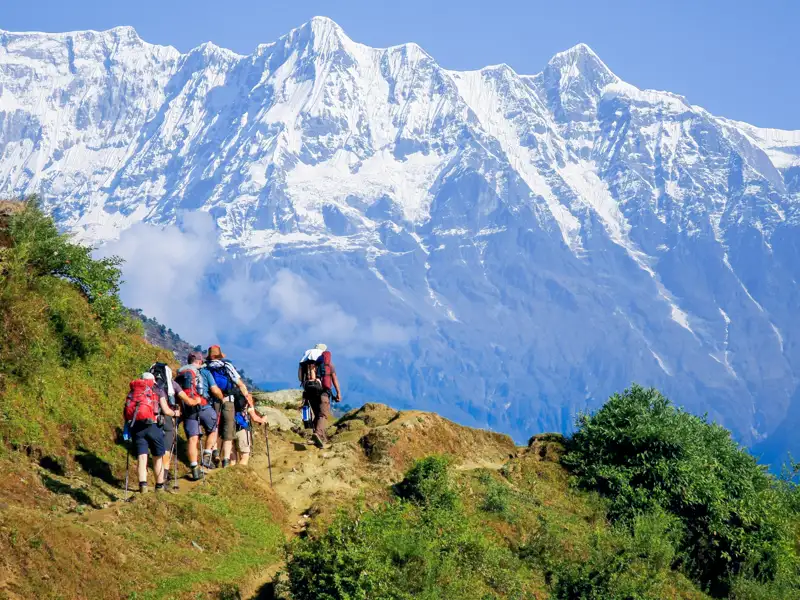 Wanderer auf einem Bergpfad inmitten einer beeindruckenden Berglandschaft mit schneebedeckten Gipfeln.