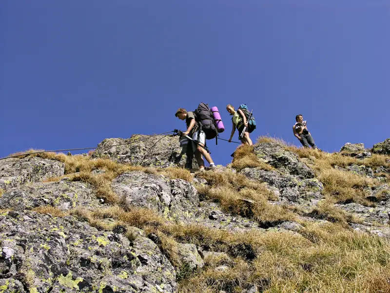 Wanderer beim Aufstieg auf einem Bergkamm mit Stahlseilsicherung.