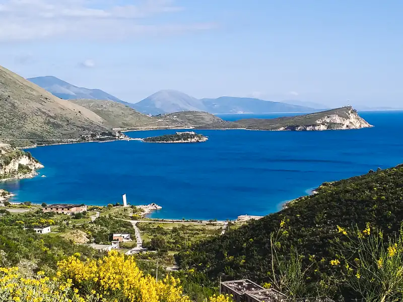 Radreise Albanien Blick auf albanische Riviera. Panorama der Küstenlandschaft mit tiefblauem Wasser, Bergen und einer kleinen Insel.