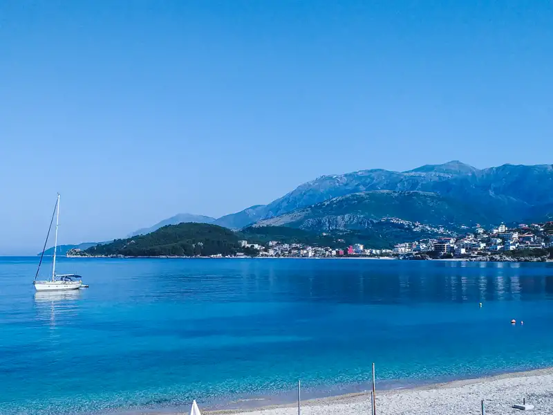 Segelboot in der Bucht vor der Küste mit Bergen im Hintergrund.
