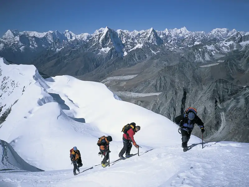 Bergsteiger mit Ausrüstung beim Aufstieg eines verschneiten Gipfels im Himalaya.