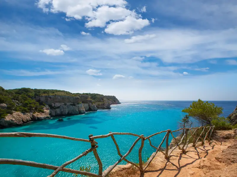Blick auf eine türkisfarbene Bucht mit einem hölzernen Geländer im Vordergrund.