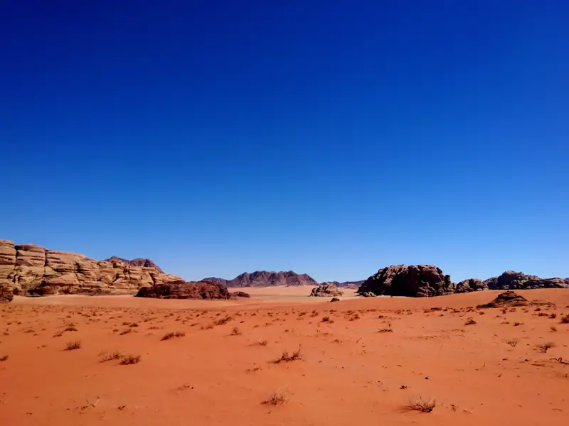 Sicht auf die rote Sandwüste mit Felsformationen und blauem Himmel.