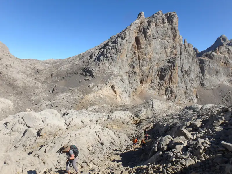 Wanderer auf einem felsigen Bergpfad, im Hintergrund ein imposanter Berggipfel.