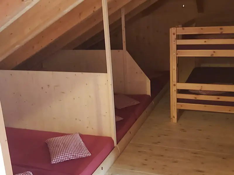 Schlafbereich im Dachgeschoss mit Einzelbetten und einem Etagenbett, ideal für Gruppen.
