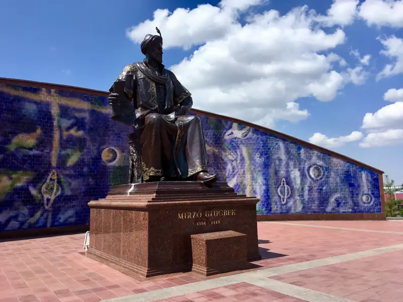 Statue von Mirzo Ulugbek mit einem blauen Mosaik im Hintergrund.