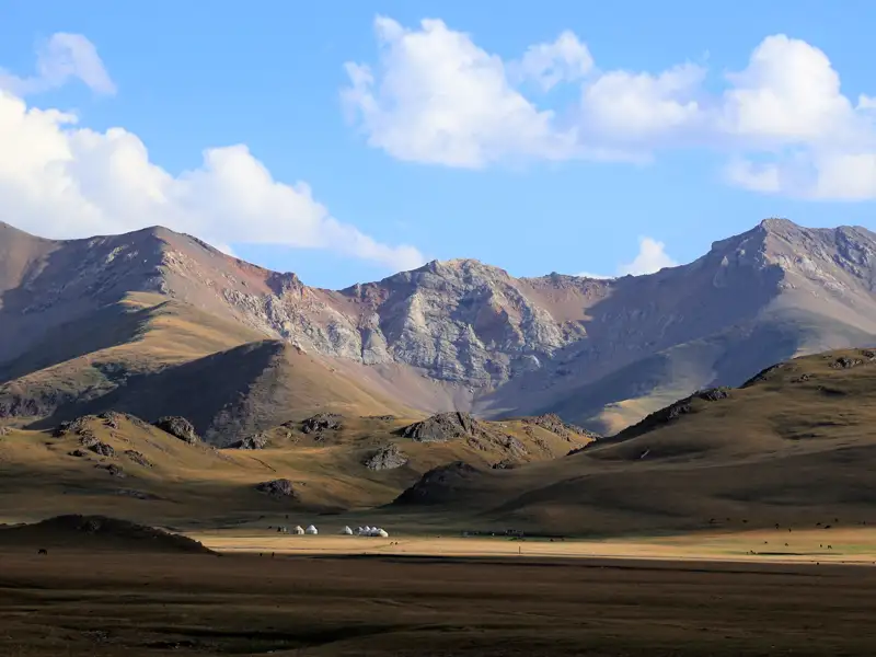 Jurtenlager in einer Hochebene mit Bergkulisse.